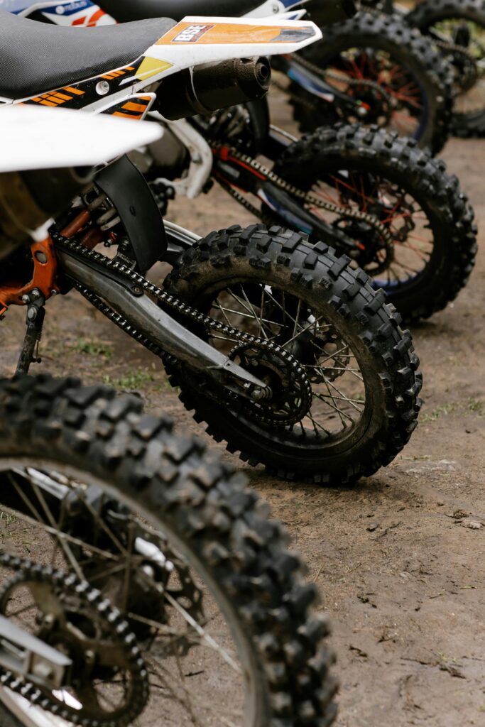 Close-up of dirt bikes parked on muddy ground, showcasing tires and chains.